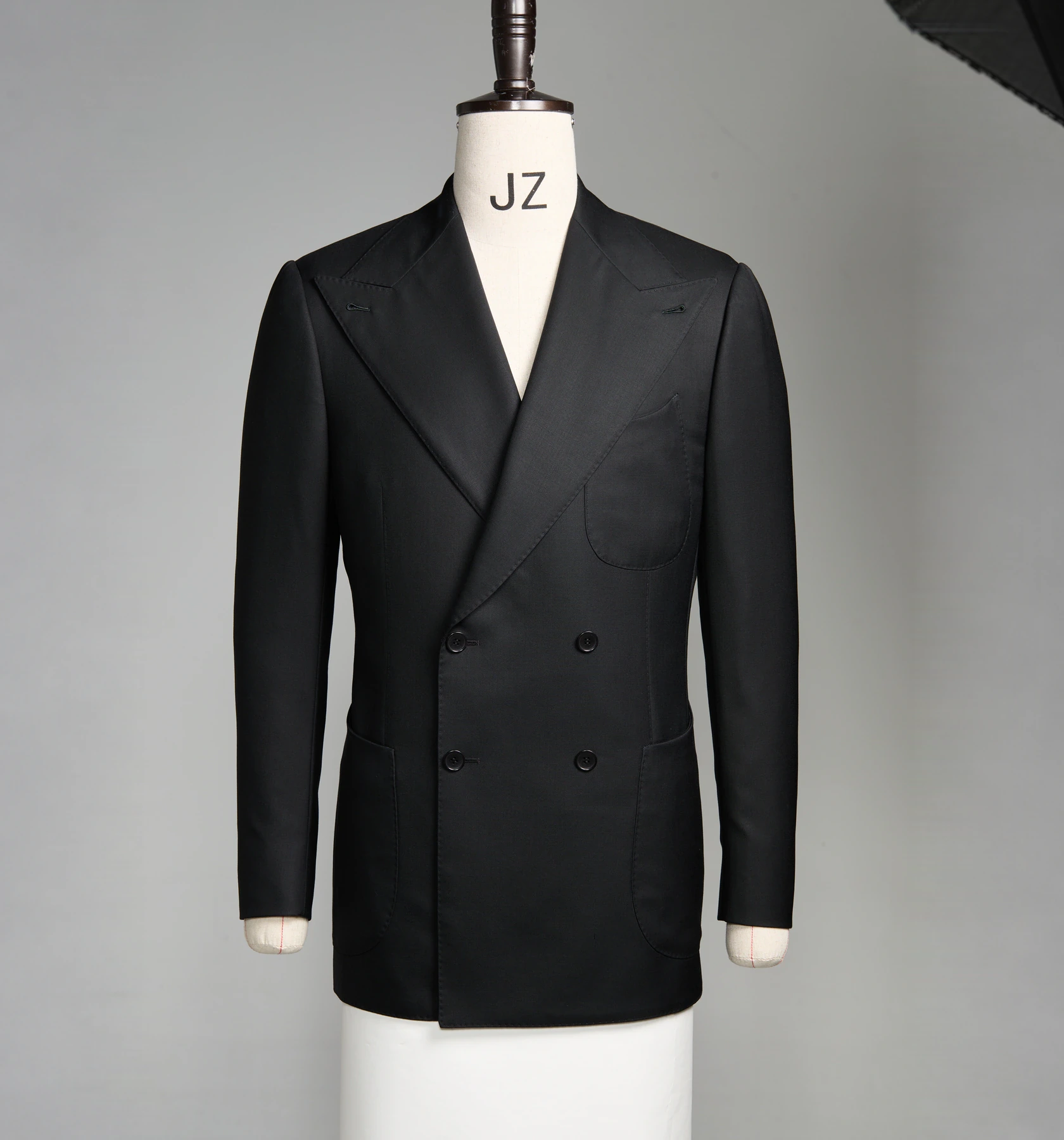 A black double-breasted bespoke jacket on a cream dress form