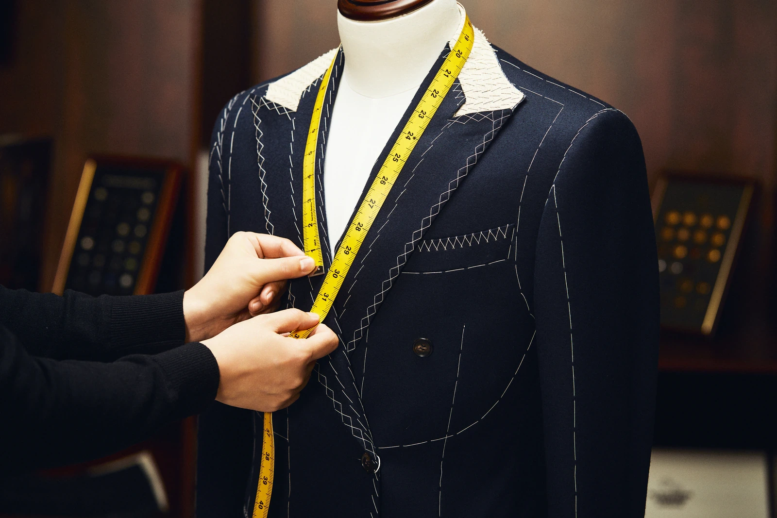 Basted navy jacket on a dress form with a measuring tape
