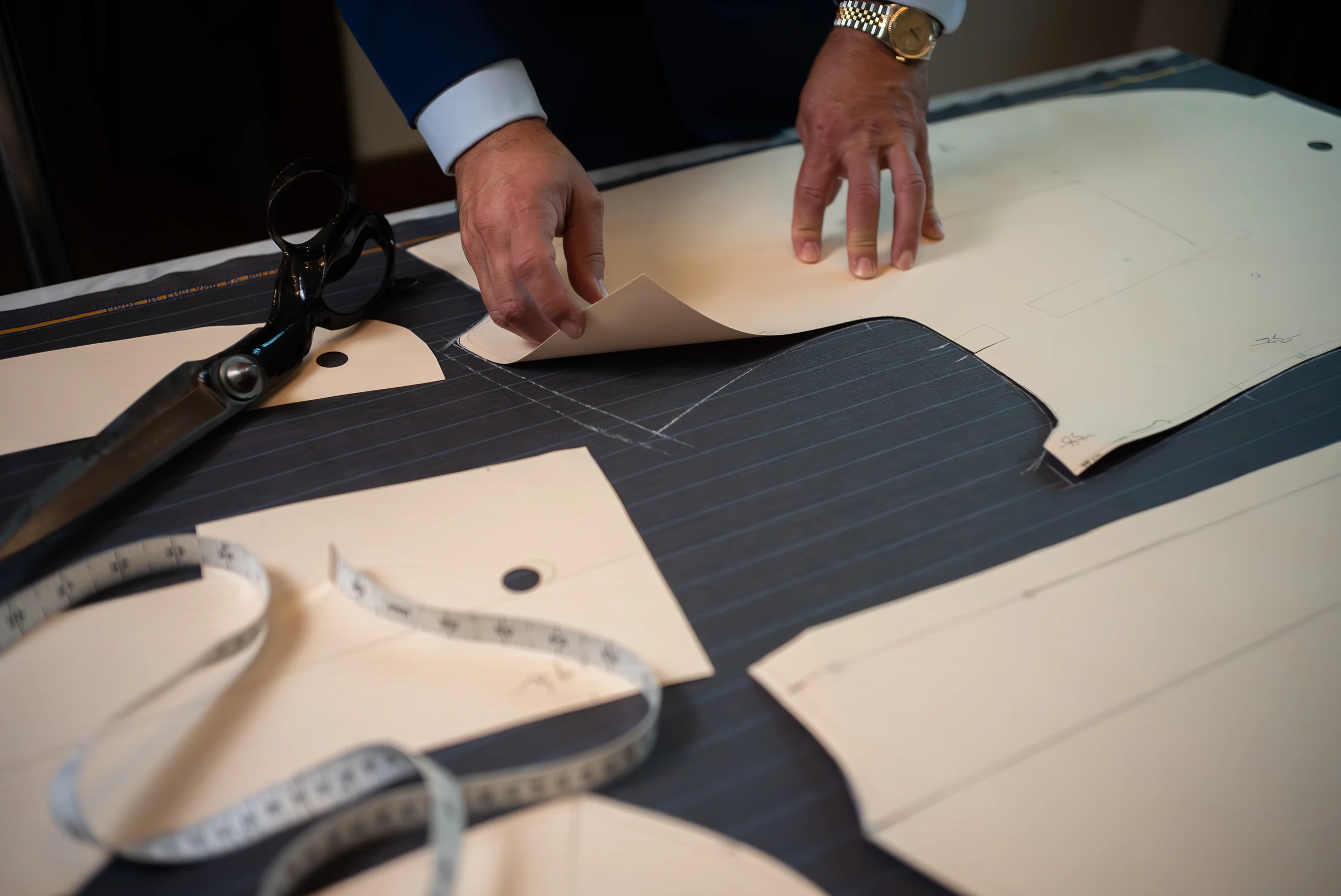 Anonymous hands drafting a jacket pattern on dark cloth