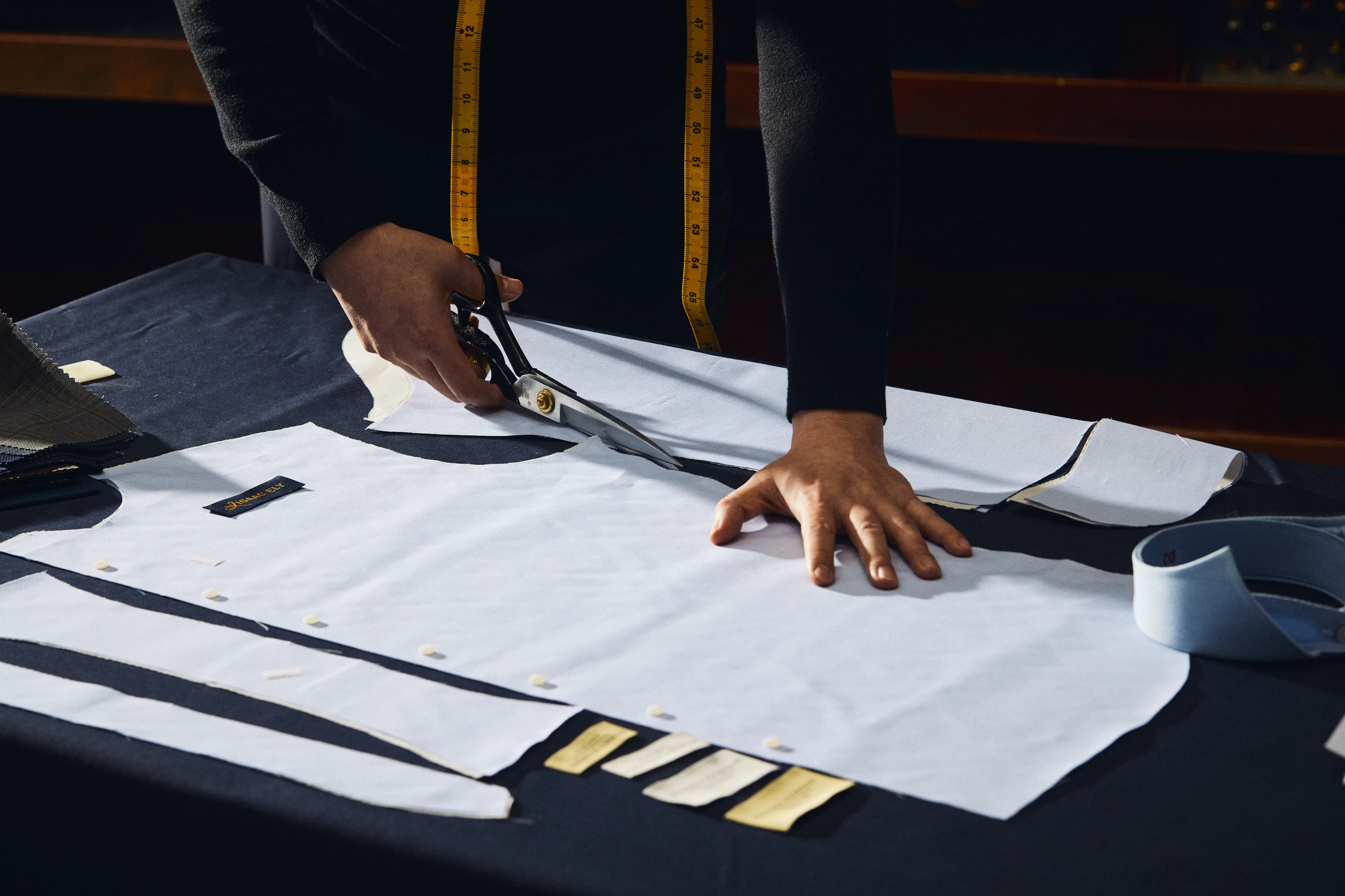A tailor measuring an anonymous client's shoulder and sleeve during a bespoke shirt fitting