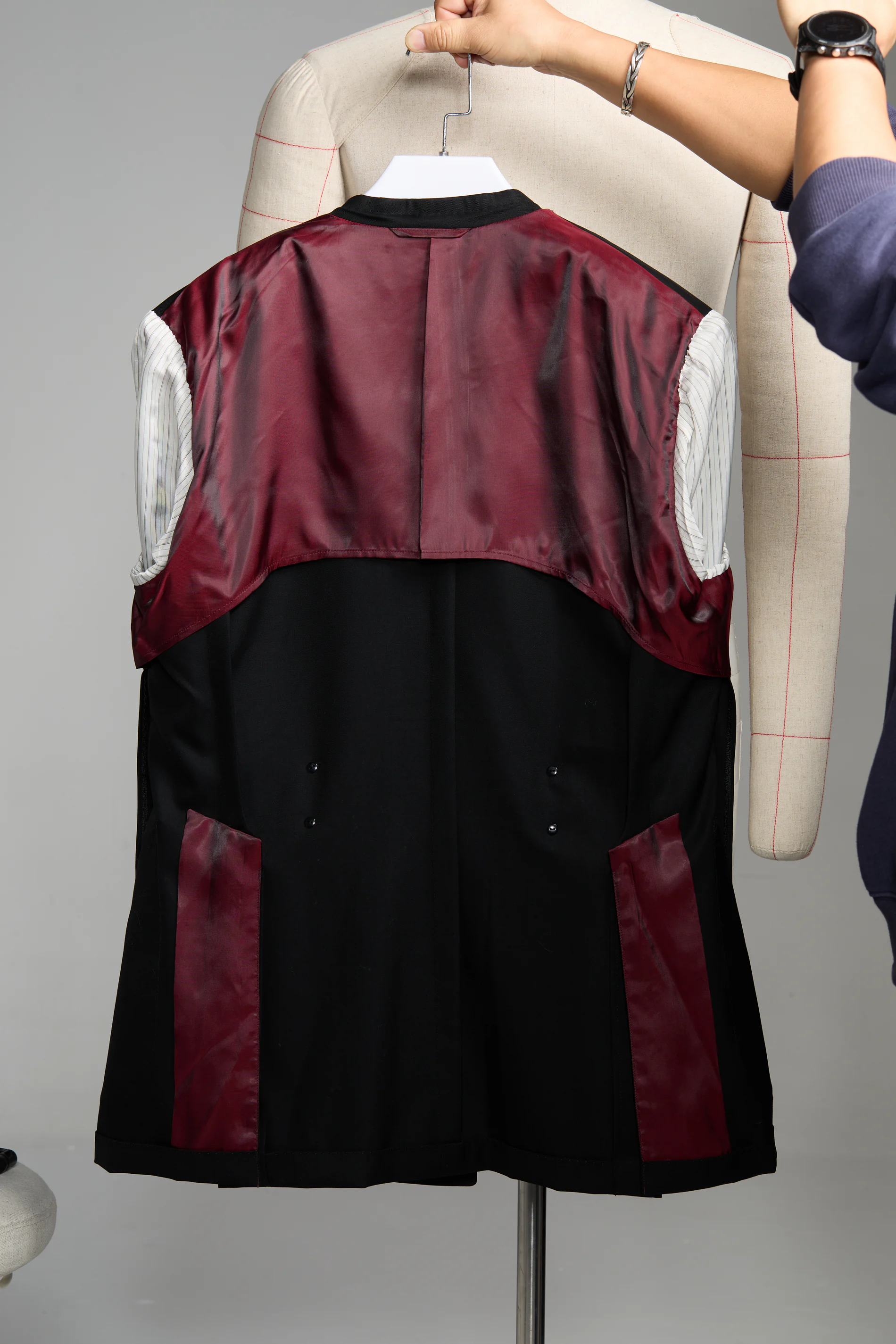 An anonymous tailor observing and adjusting the shoulder balance of a client's basted jacket