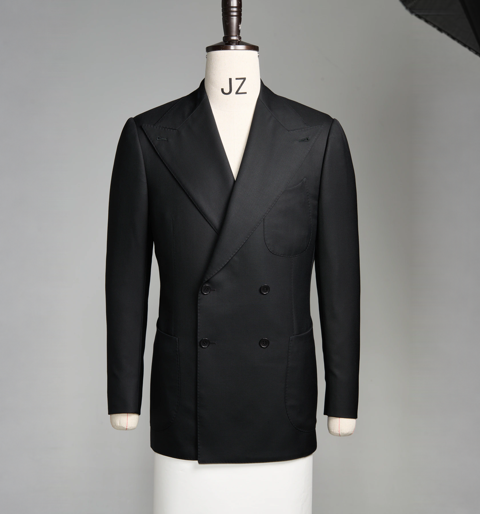 A black double-breasted bespoke jacket on a cream dress form