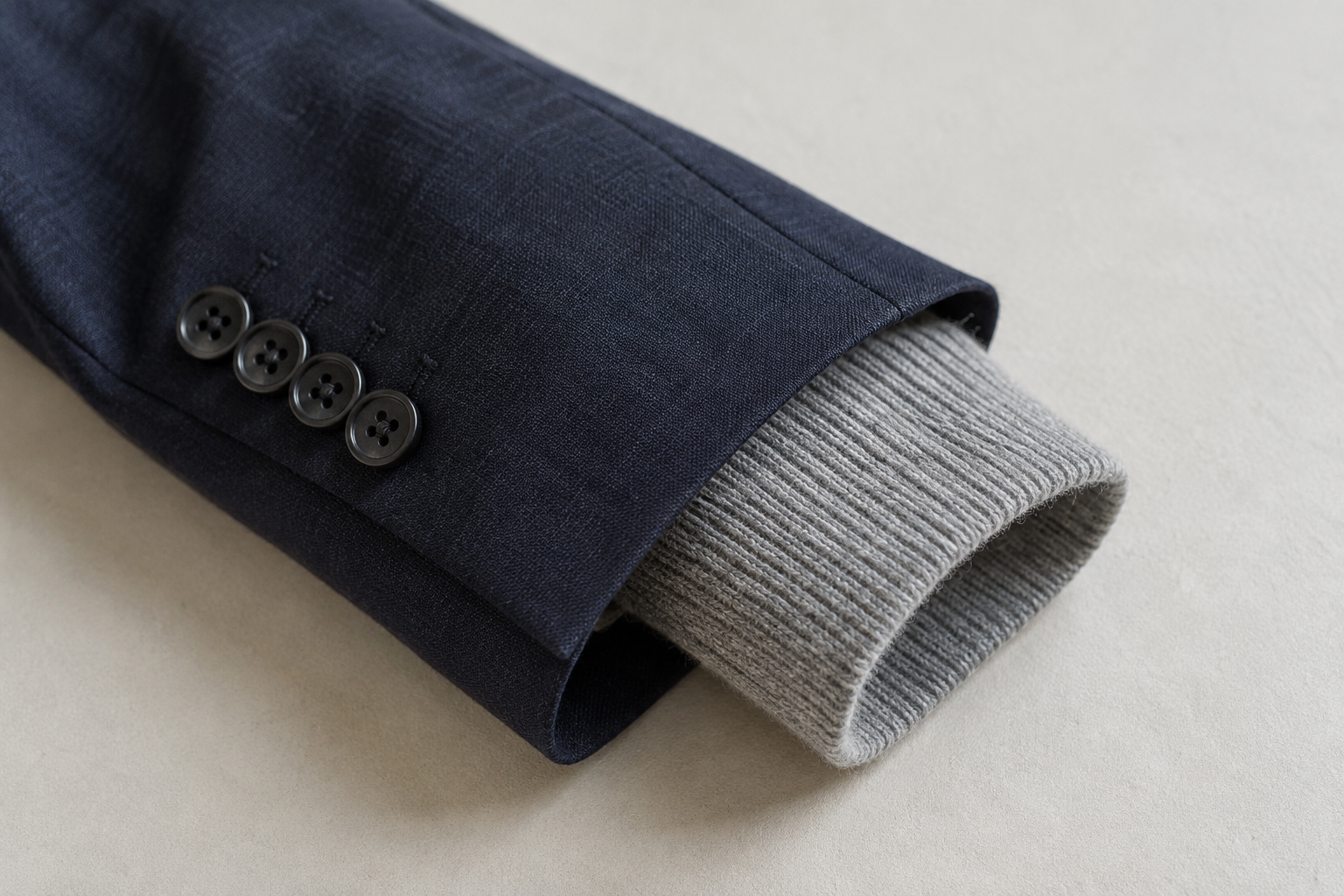 Ribbed grey knit cuff extending from a navy jacket sleeve on a pale surface