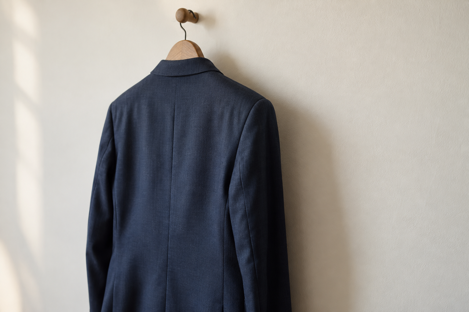 Back and sleeve of a navy suit jacket hanging from a wooden hanger
